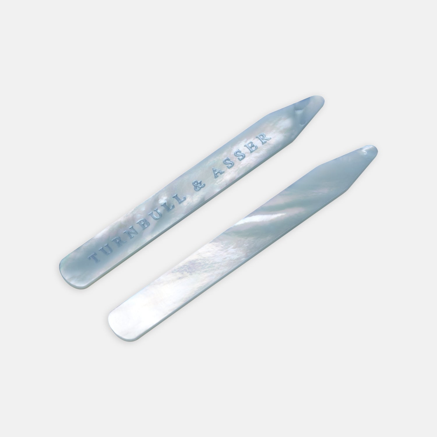 View 1 of product Two blue mother-of-pearl collar stays by Turnbull & Asser, ideal for keeping your shirt collar crisp; one is engraved with the brand name and both are displayed on a light gray background.