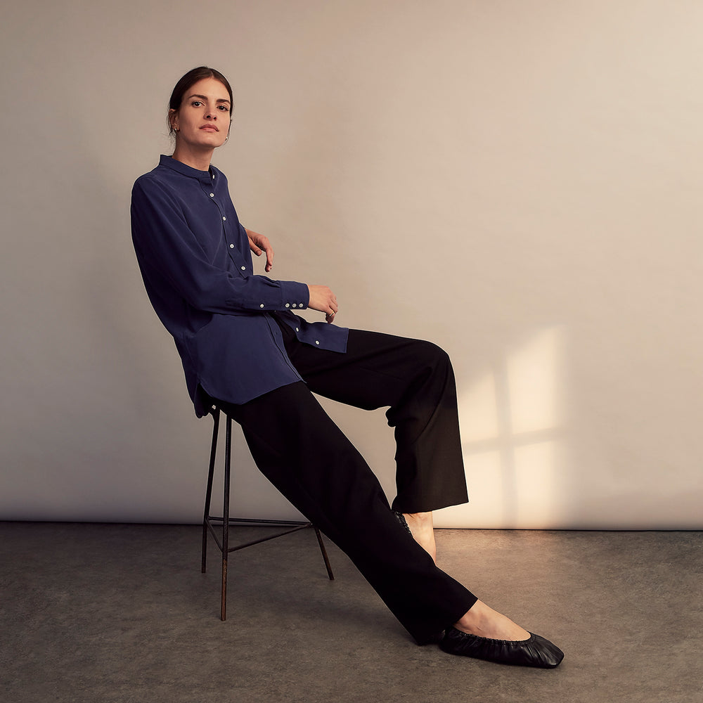 The Turnbull & Asser Blue Soft-touch Silk Lauren Shirt is a navy, long-sleeve button-up with an Igret stand collar, white buttons, curved hem, relaxed fit, and elongated body for a modern look, shown laid flat on a white background.