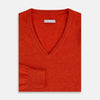 View 4 of product The Turnbull & Asser Red Orange Cashmere V-neck Jumper features long sleeves, ribbed cuffs and hem, displayed on a plain white background—a stylish knitwear essential for any wardrobe.