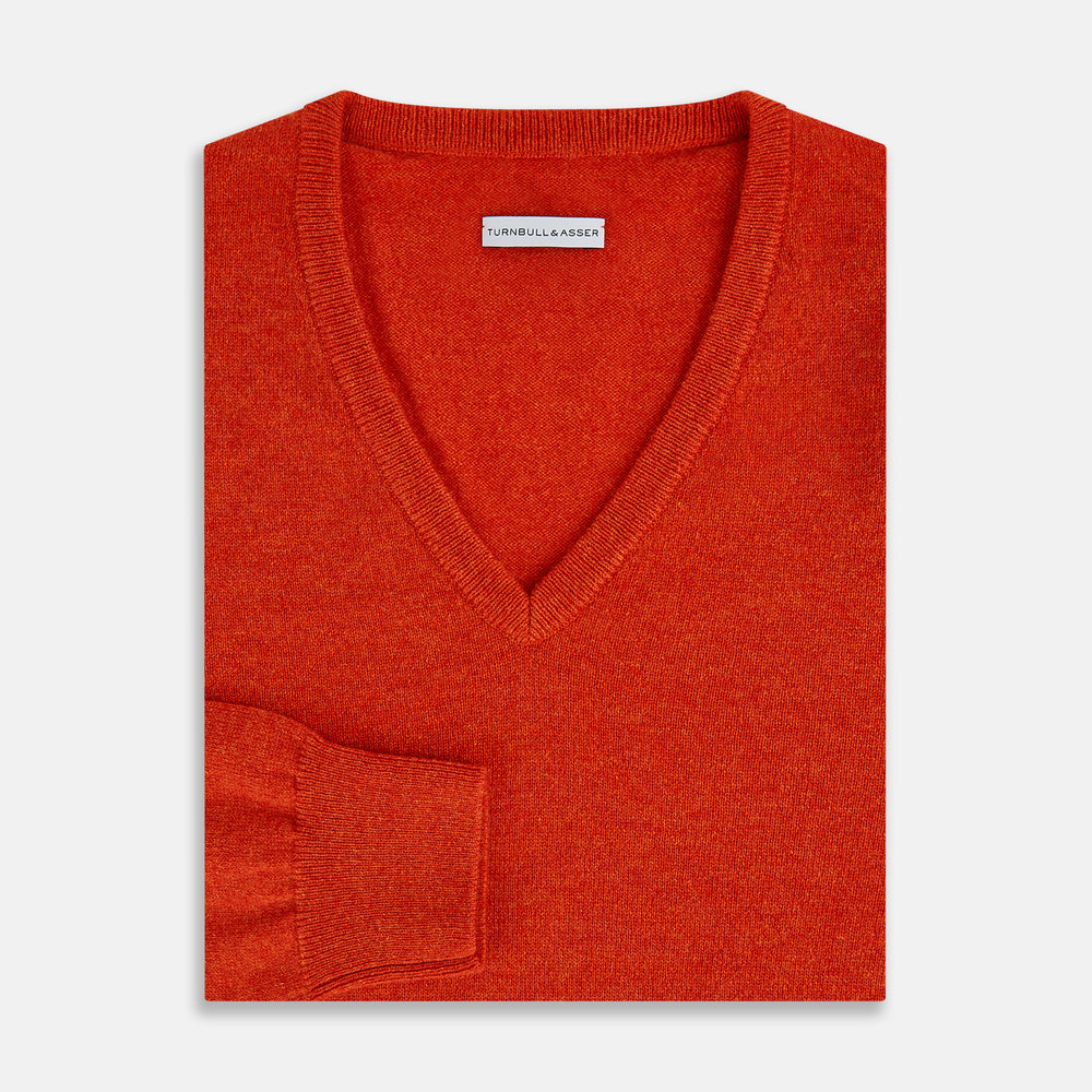 The Turnbull & Asser Red Orange Cashmere V-neck Jumper features long sleeves, ribbed cuffs and hem, displayed on a plain white background—a stylish knitwear essential for any wardrobe.