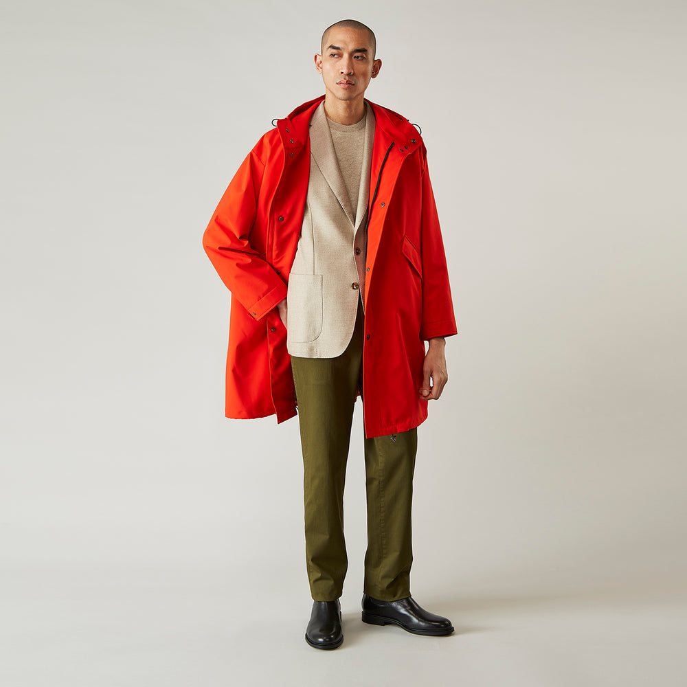 Wearing the Turnbull & Asser Red Walter Sealup Parka with Detachable Liner, black pants, and white sneakers, a person stands in profile against a plain light background—perfect for travel.