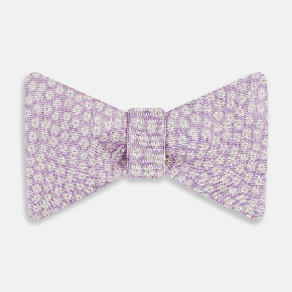 The Turnbull & Asser Lilac Flower Patterned Silk Bow Tie showcases small white flowers on lilac silk, making it a refined accessory for smart outfits. Shown against a white background.