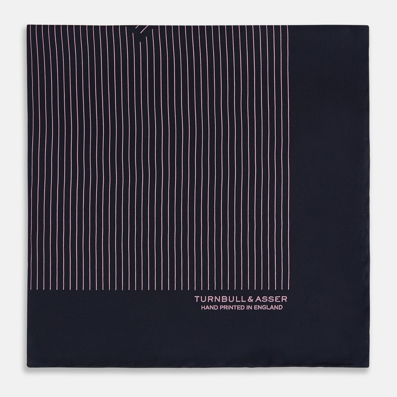 View 4 of product The Navy and Pink Stripe Silk Pocket Square by Turnbull & Asser features thin pink stripes, a geometric border, hand-rolled edges, and "TURNBULL & ASSER HAND PRINTED IN ENGLAND" printed in white.