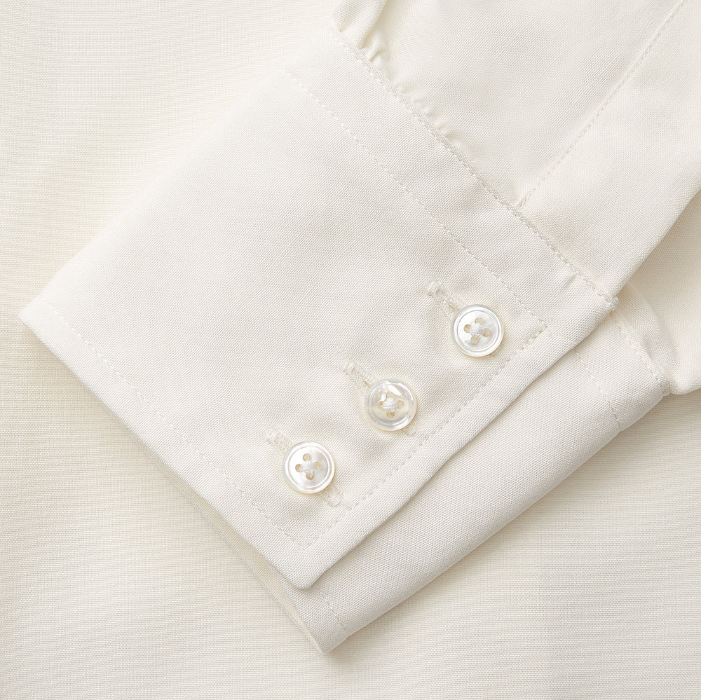The Cream Silk Tailored Bianca Shirt by Turnbull & Asser features long sleeves, a pointed collar, and curved hem in soft-touch peace silk with a tailored fit. Shown laid flat on a white background.