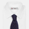 View 2 of product The Turnbull & Asser LACE ON TONE SPOT NAVY TULIP RED TIE is a classic men's accessory crafted from textured navy fabric with small red polka dots, neatly rolled with the pointed end facing forward.
