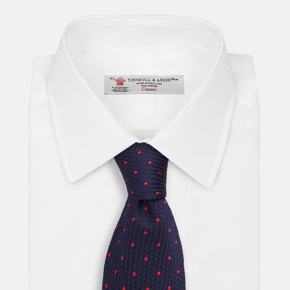 The Turnbull & Asser LACE ON TONE SPOT NAVY TULIP RED TIE is a classic men's accessory crafted from textured navy fabric with small red polka dots, neatly rolled with the pointed end facing forward.