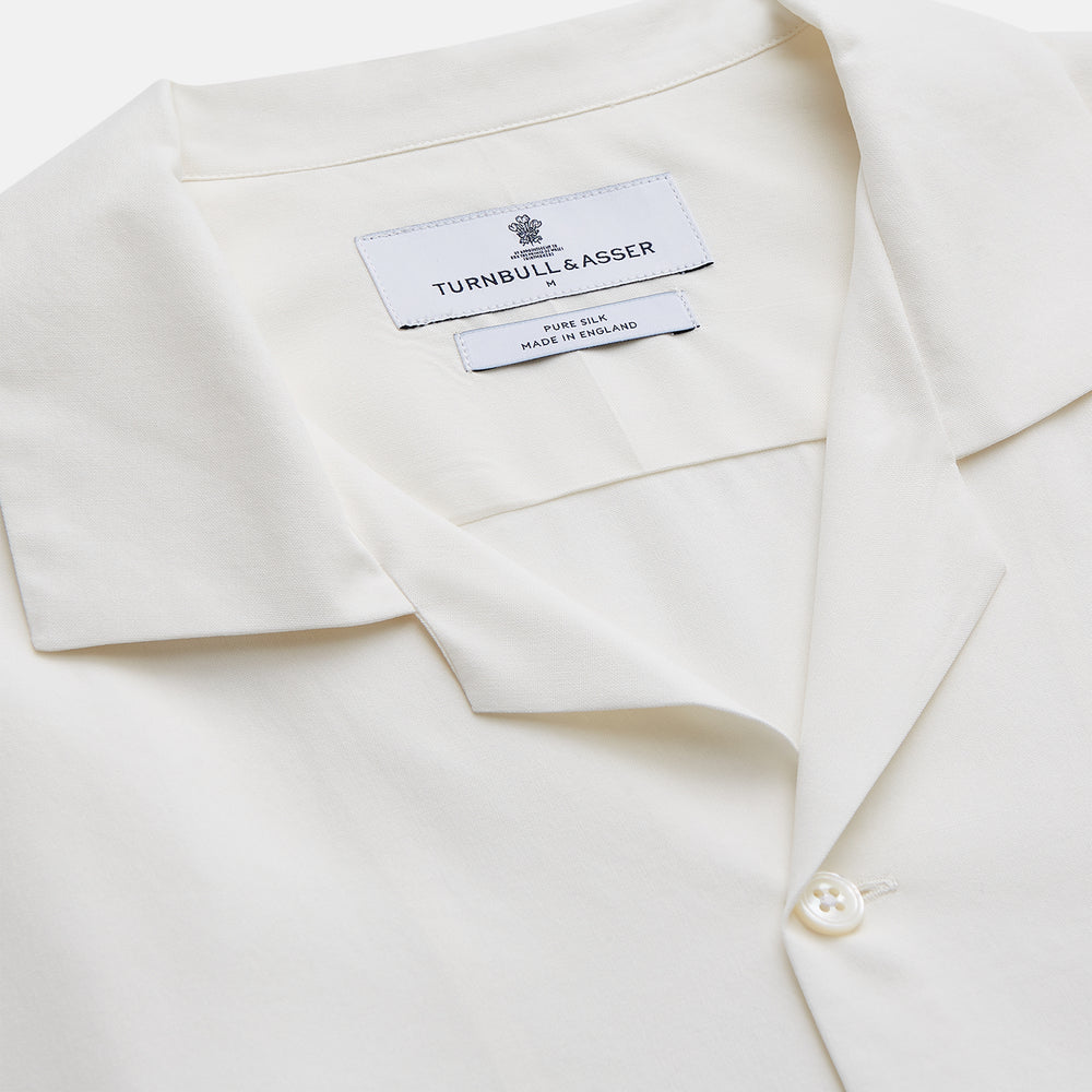 The Cream Silk Holiday Fit Phillips Shirt by Turnbull & Asser is a short-sleeved, collared silk shirt in off-white with three front pockets and a revere collar, displayed flat on a plain white background.