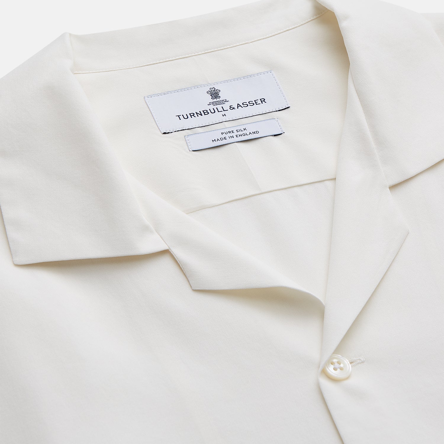 View 2 of product The Cream Silk Holiday Fit Phillips Shirt by Turnbull & Asser is a short-sleeved, collared silk shirt in off-white with three front pockets and a revere collar, displayed flat on a plain white background.