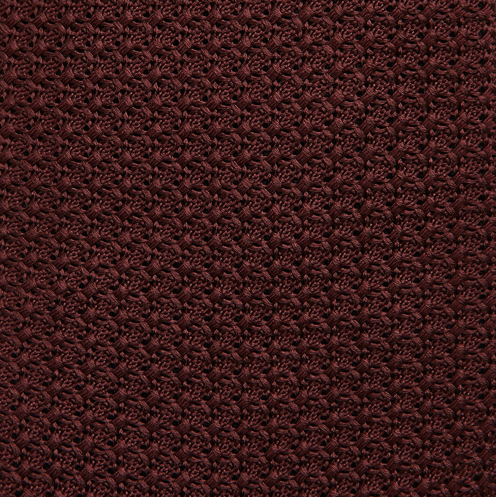 The Turnbull & Asser Burgundy Knitted Tie, rolled and featuring a textured pattern, is displayed on a plain white background—a refined accessory ideal for the modern gentleman’s wardrobe.