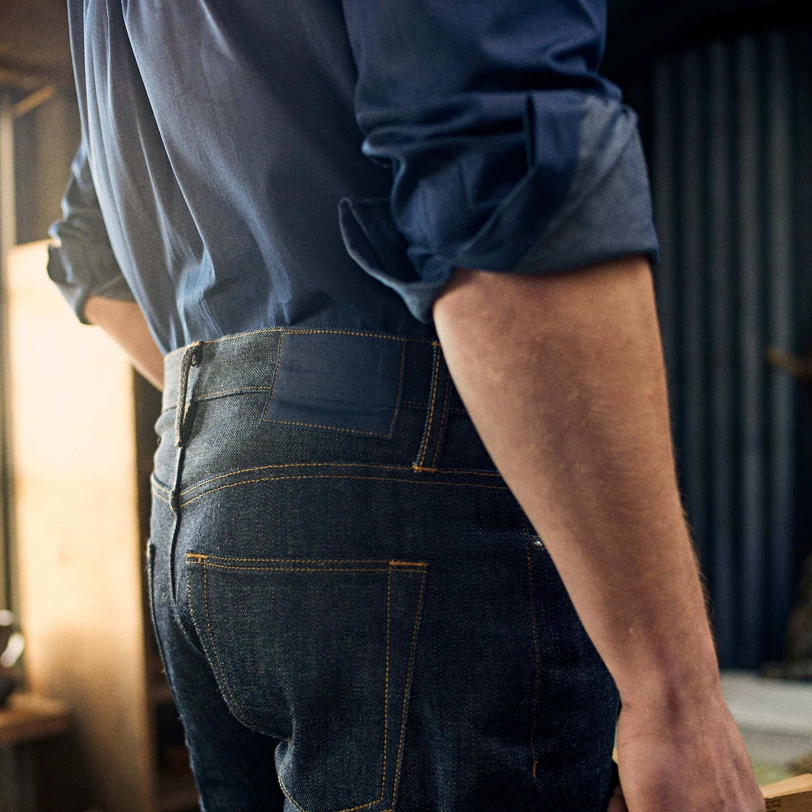 View 2 of product A pair of Turnbull & Asser Indigo Japanese Selvedge Denim Jeans in dark blue with rolled-up cuffs, yellow stitching, five pockets, and a button fly, laid flat on a white background.