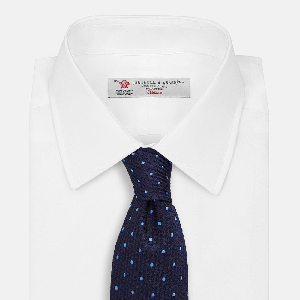 The LACE ON TONE SPOT NAVY FORD TIE by Turnbull & Asser is a rolled-up navy tie with textured fabric and an evenly spaced pattern of small light blue polka dots.