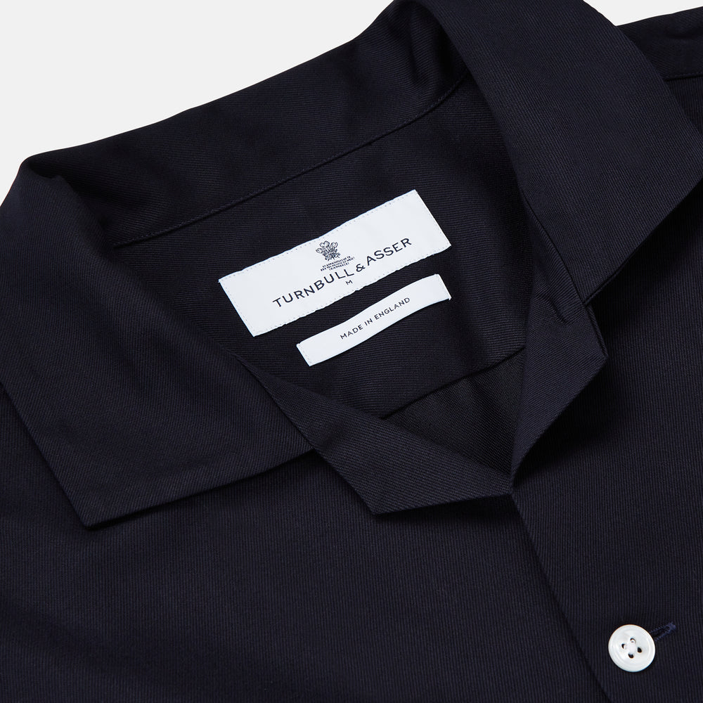 A Navy Cotton Holiday Fit Winnington Shirt by Turnbull & Asser, featuring long sleeves, a chest pocket, white buttons, and a revere collar, is laid flat on a white background.