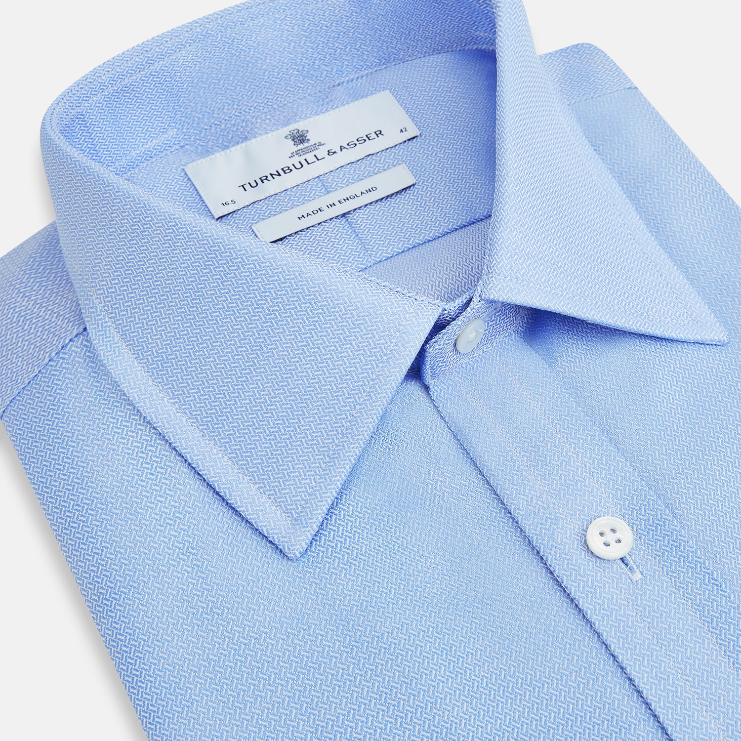 View 2 of product The Blue Herringbone Mayfair Shirt by Turnbull & Asser features light blue and white stripes, long sleeves, a classic collar, white buttons, and buttoned cuffs. Shown on a plain white background, it's perfect for formal occasions.