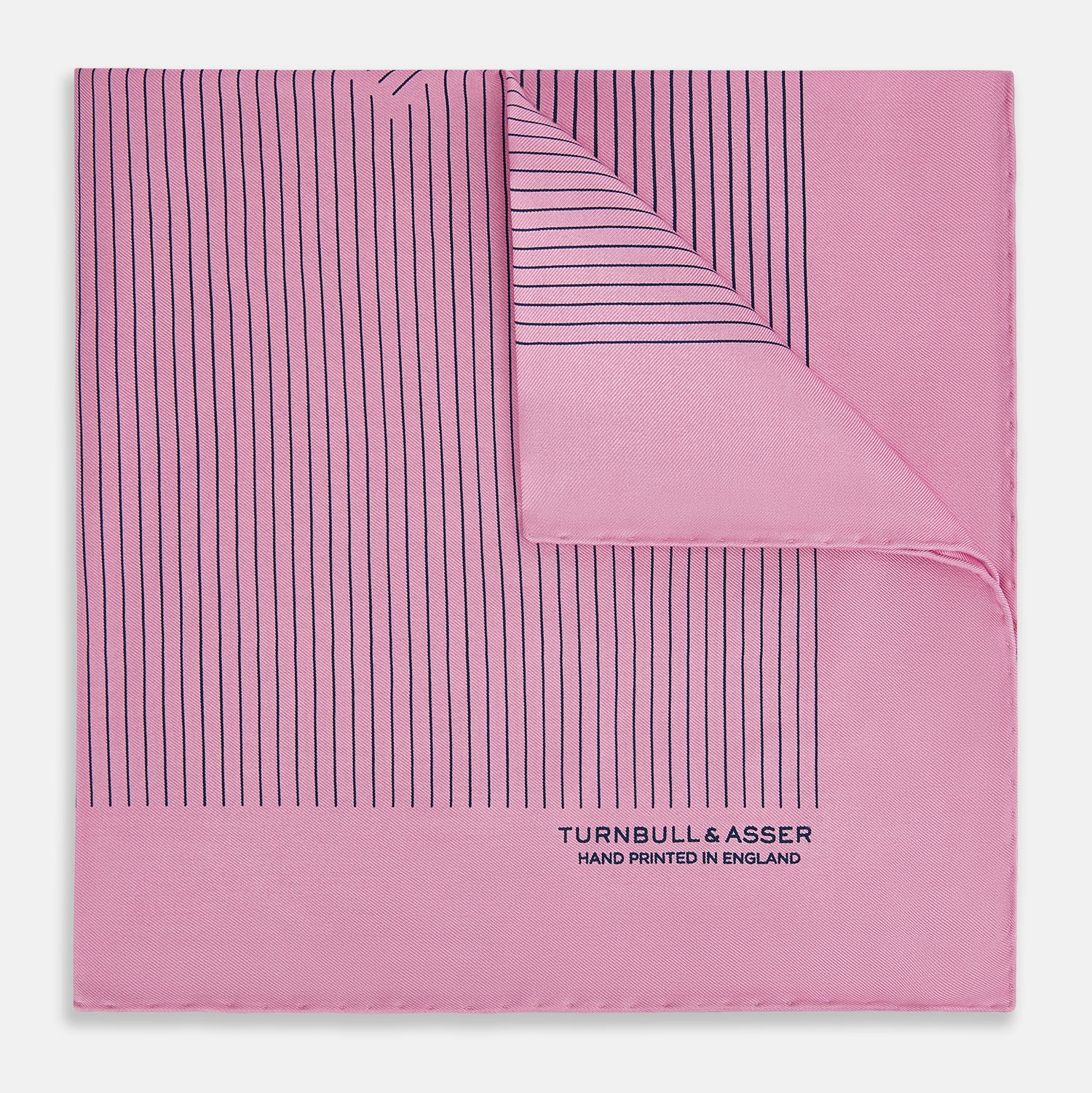 View 1 of product The Turnbull & Asser Pink Stripe Silk Pocket Square features thin vertical navy stripes and "TURNBULL & ASSER HAND PRINTED IN ENGLAND" in the bottom right corner, with one corner stylishly folded over.