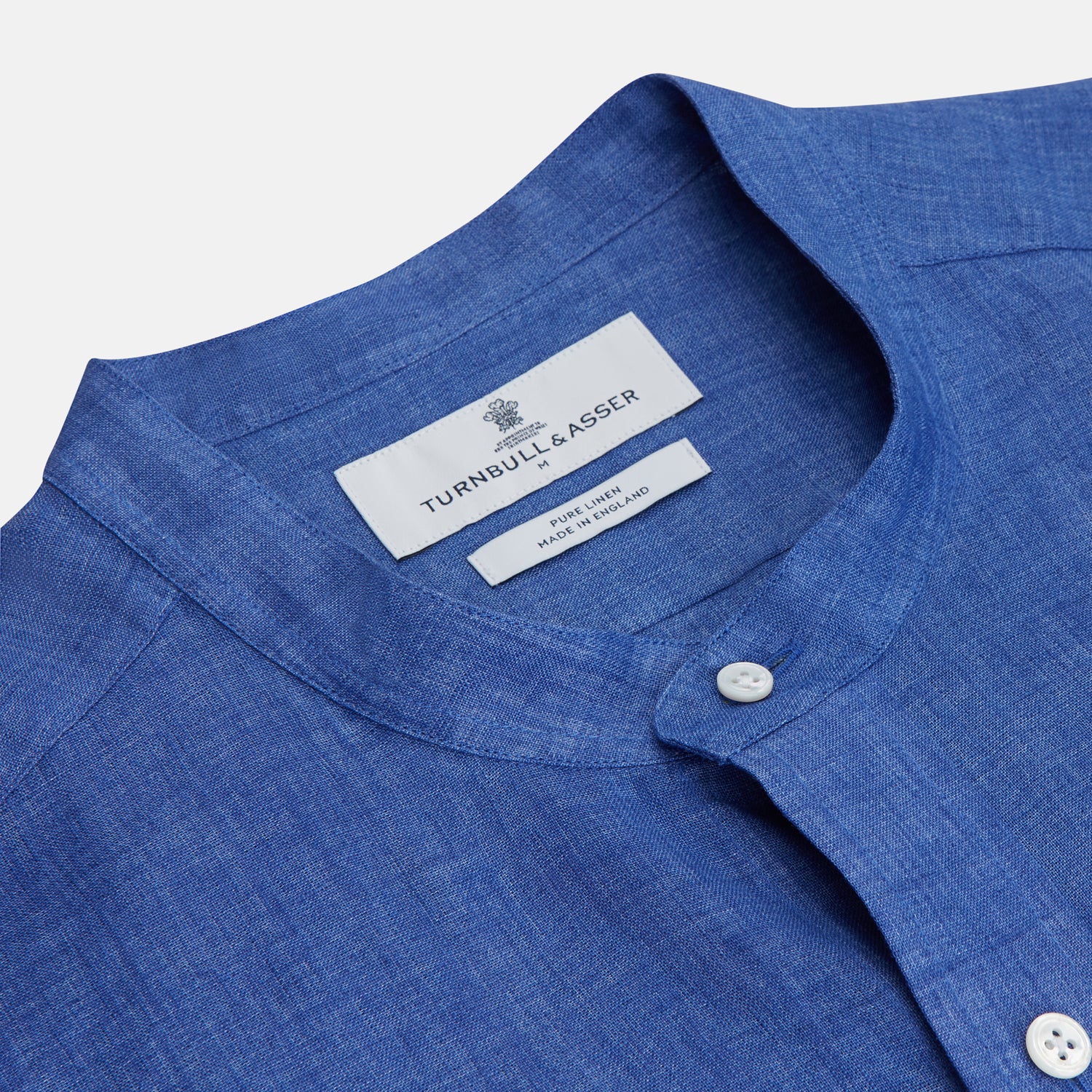 View 5 of product A man faces forward with a neutral expression, hands in his pockets, wearing the Turnbull & Asser Plain Indigo Linen Weekend Fit Shirt with a stand collar, styled with dark pants and black shoes against a plain light background.