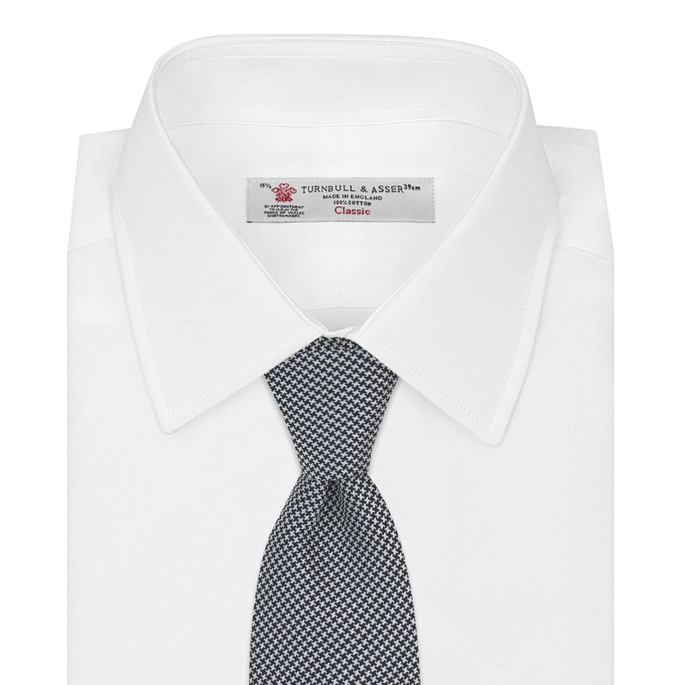 The Turnbull & Asser White and Black Houndstooth Woven Silk Tie, shown rolled on a light grey background, adds a classic touch to any smart outfit.
