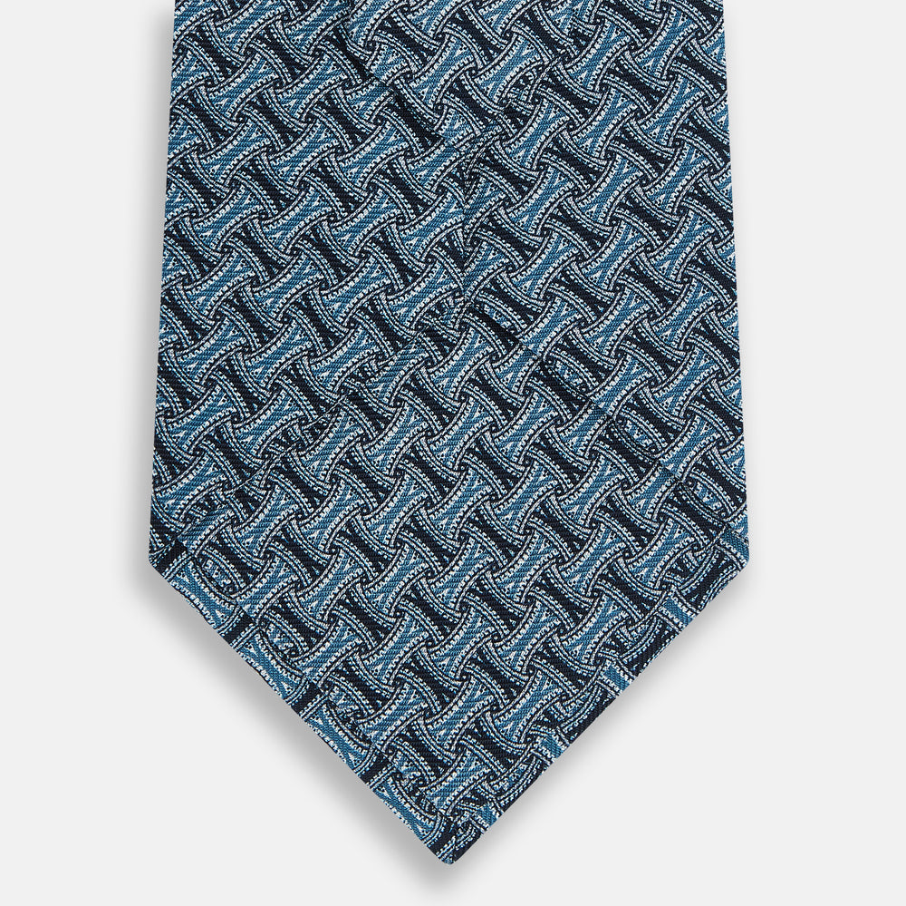 A close-up of the Turnbull & Asser Pale Blue and Navy Weave Patterned Silk Tie, featuring a textured geometric design. The silk tie is rolled at one end and displayed on a white background.