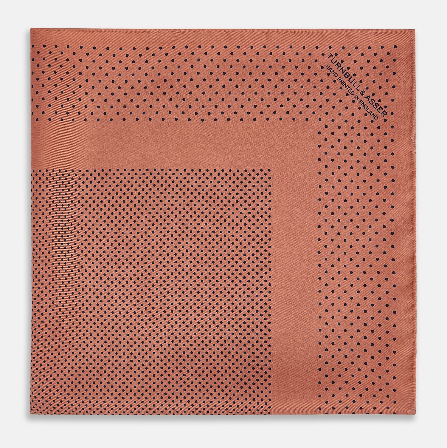 View 3 of product The Turnbull & Asser Blush Dot Silk Pocket Square features a rust hue with black polka dots, a bordered design, and hand-rolled edges, shown folded against a white background.