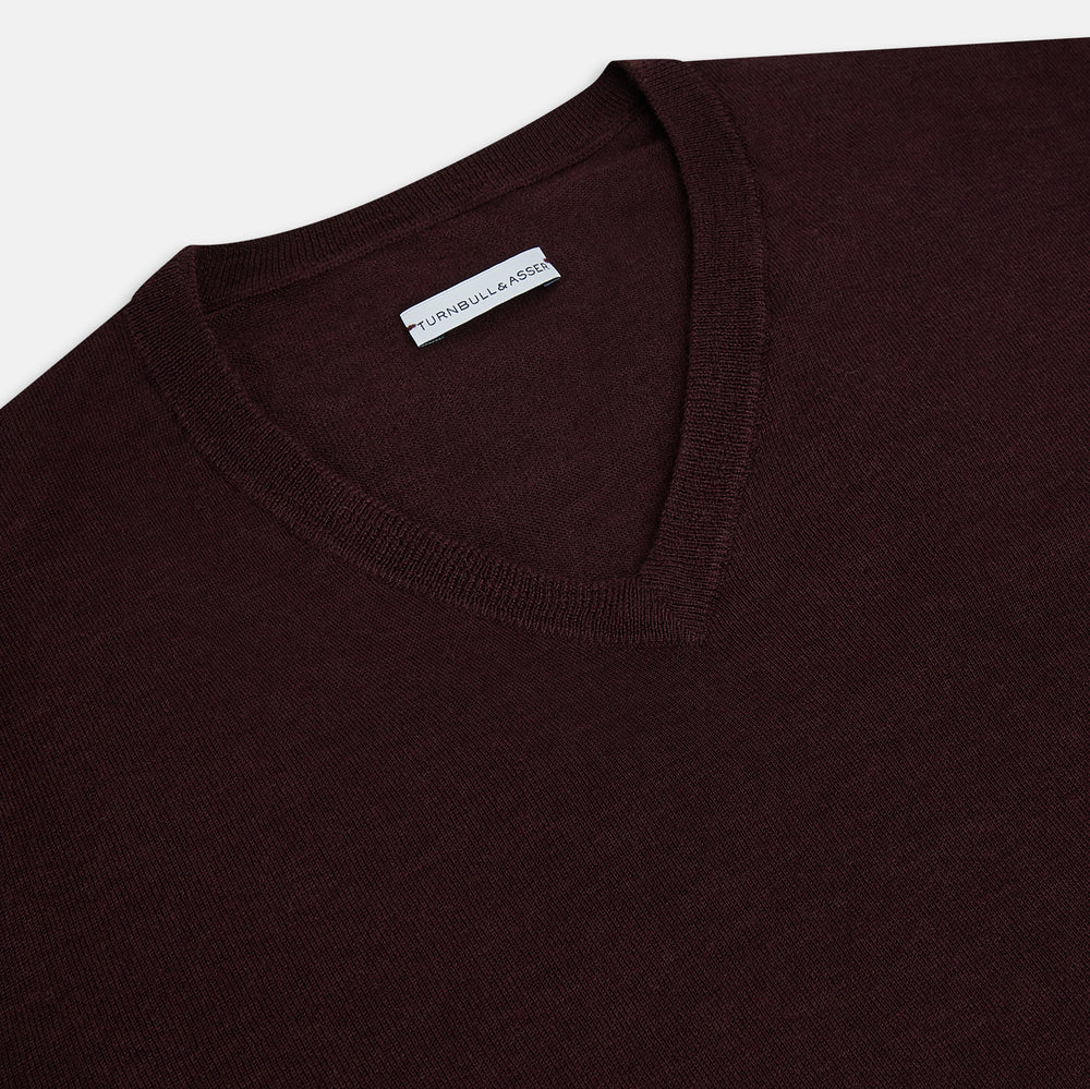 The Turnbull & Asser Burgundy Fine Merino V-Neck Jumper features a classic plain knit design with long sleeves, showcased against a crisp white background.