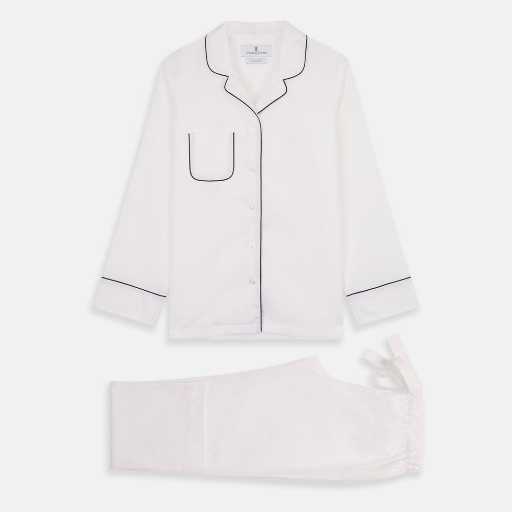 The Turnbull & Asser Women's Harriet Plain White Cotton Pyjama Set features long sleeves, black piping, a chest pocket, and matching pants with elastic waistband and ribbon tie, all displayed on a white background.
