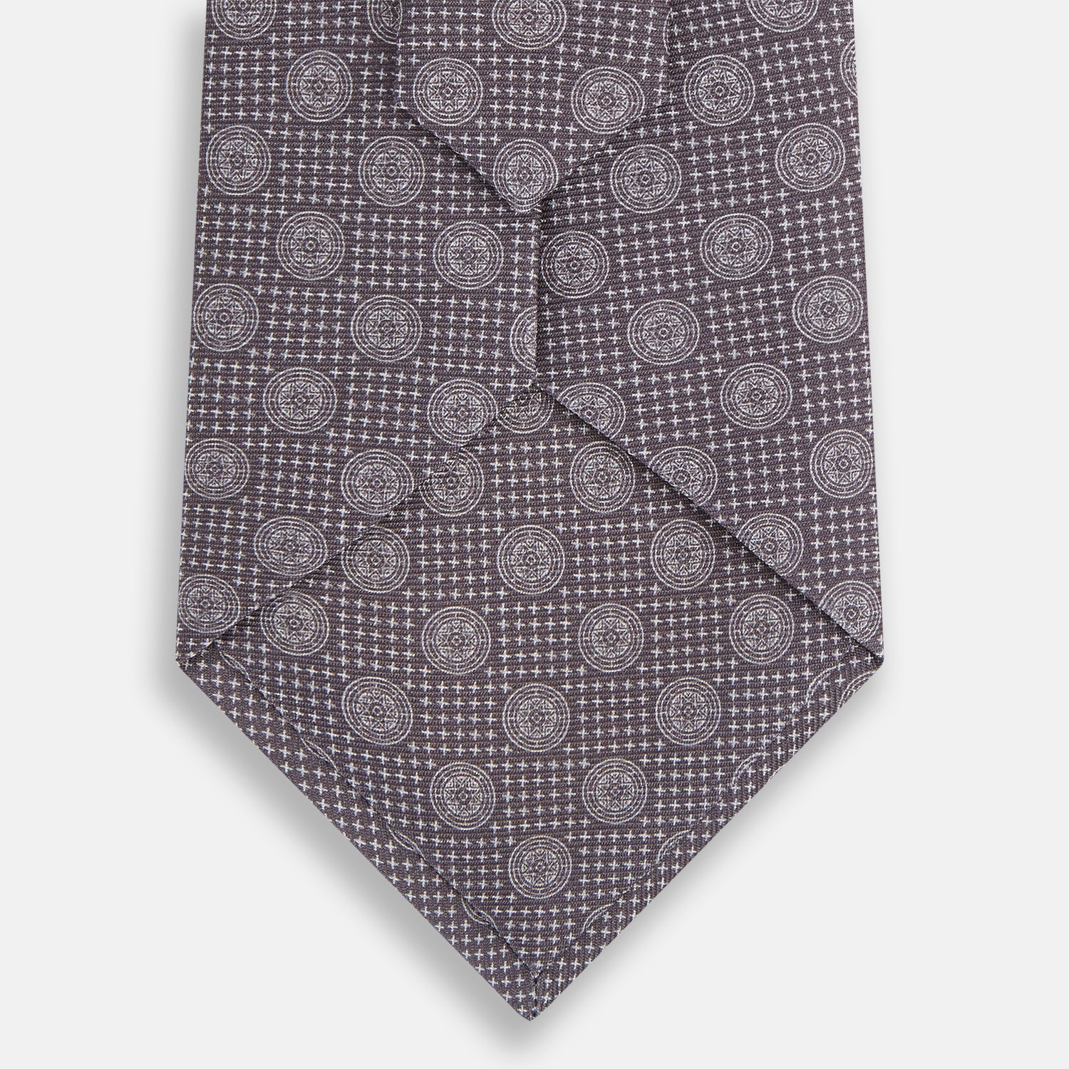 View 3 of product The Turnbull & Asser Ash Medallion Silk Tie features rolled-up ash silk with gray and light purple medallion and grid-like motifs on a white background.