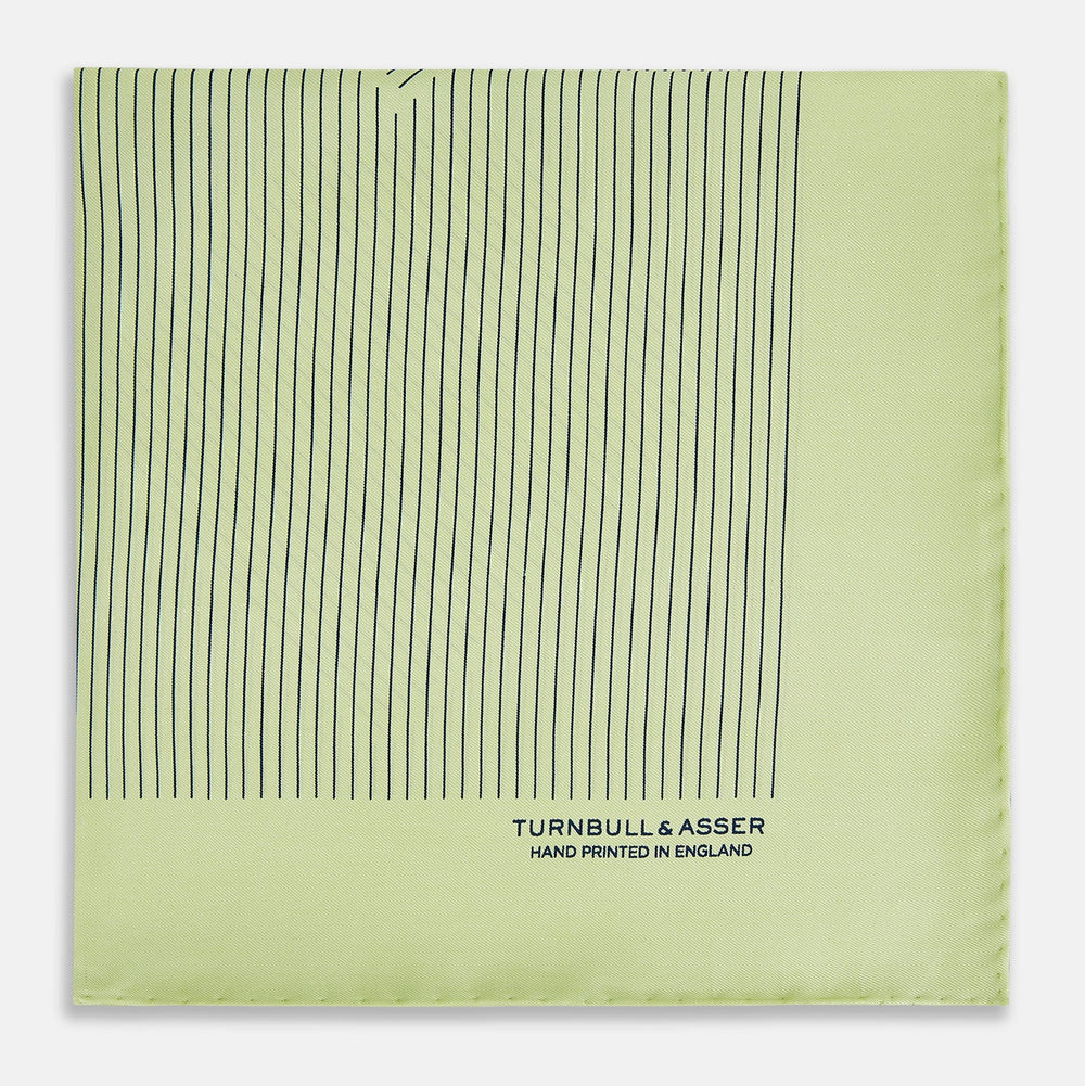 The Melon Green Stripe Silk Pocket Square by Turnbull & Asser features thin vertical black lines on light green silk, neatly folded to display both sides. The lower corner reads “TURNBULL & ASSER HAND PRINTED IN ENGLAND.”.