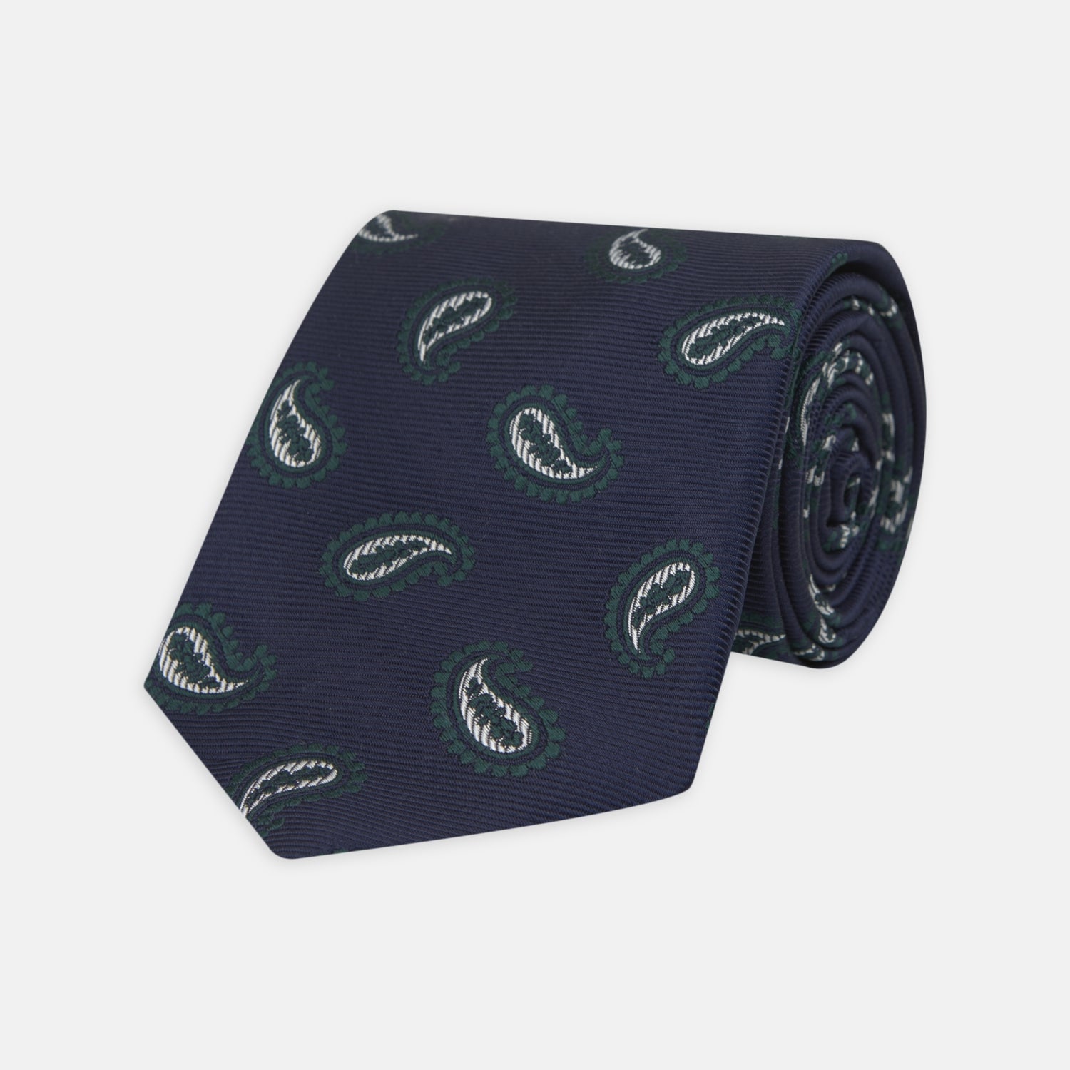 View 1 of product The Turnbull & Asser Navy and Forest Green Floating Paisley Silk Tie features a green and white paisley pattern, elegantly rolled up for a stylish presentation.