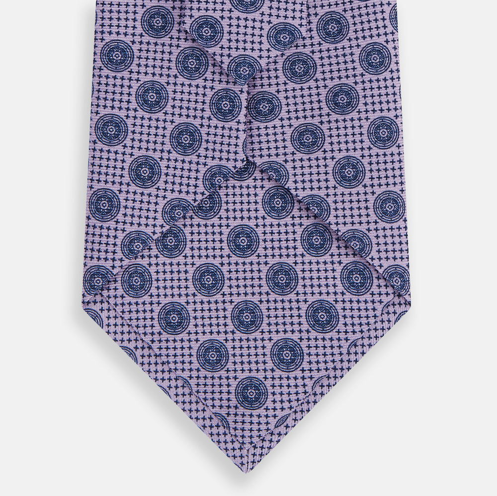 The Turnbull & Asser Lilac Medallion Silk Tie features a repeating navy medallion motif on textured lilac silk, adding refined style to any ensemble.