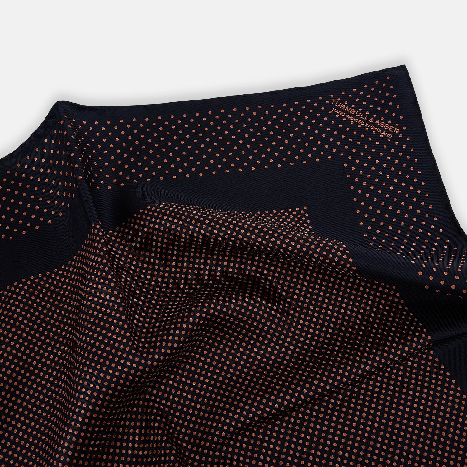 View 2 of product The Navy and Blush Dot Silk Pocket Square by Turnbull & Asser features a navy base with small orange polka dots and a border, shown neatly folded with one corner flipped over.