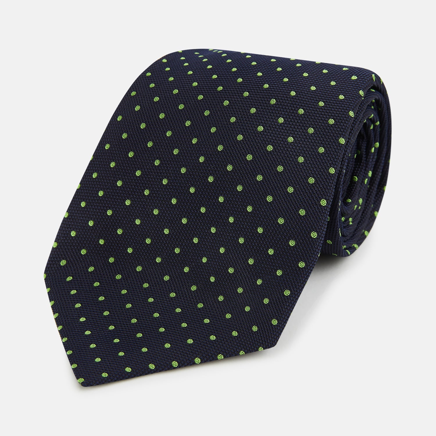 View 1 of product The Turnbull & Asser Green and Navy Micro Dot Silk Tie features small green dots on a navy silk background, displayed rolled up on white.