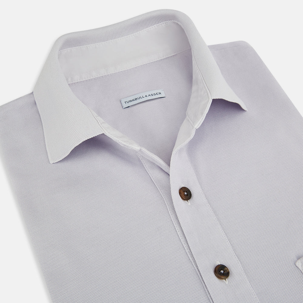 A soft pink cotton polo shirt by Turnbull & Asser features short sleeves, a contrasting white collar, three dark buttons, and a left chest pocket. Laid flat on a white background—it’s perfect for modern men’s fashion.