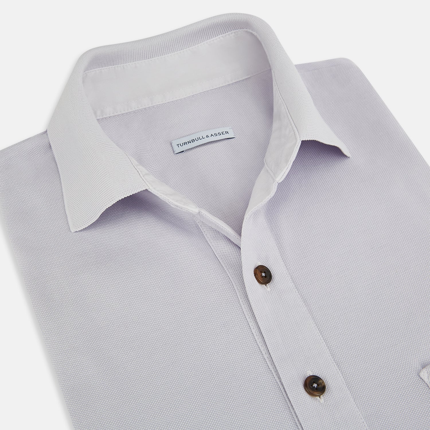 View 2 of product A soft pink cotton polo shirt by Turnbull & Asser features short sleeves, a contrasting white collar, three dark buttons, and a left chest pocket. Laid flat on a white background—it’s perfect for modern men’s fashion.