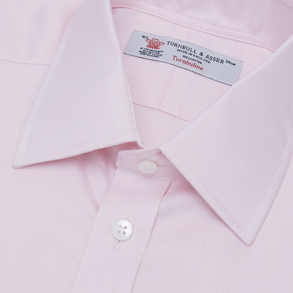 The Turnbull & Asser Pink Herringbone Superfine Cotton Shirt features a T&A collar, double cuffs, and clean-cut design, displayed neatly folded against a white background.