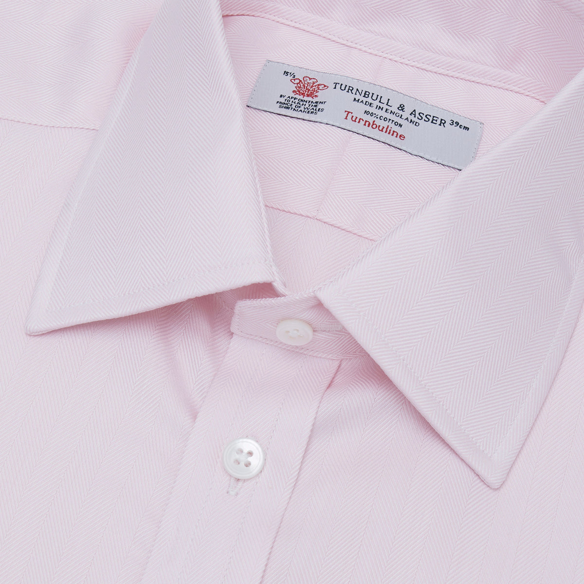 View 5 of product The Turnbull & Asser Pink Herringbone Superfine Cotton Shirt features a T&A collar, double cuffs, and clean-cut design, displayed neatly folded against a white background.