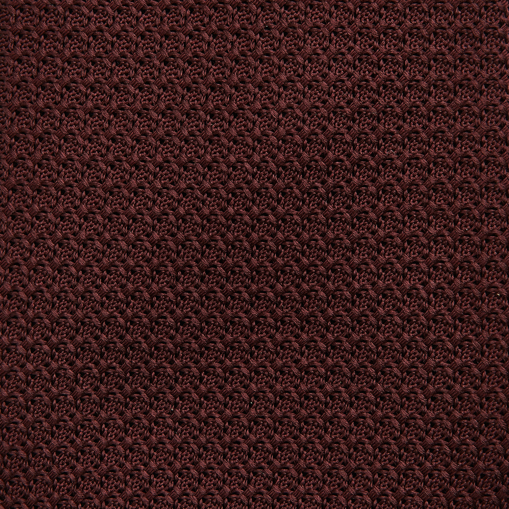The Turnbull & Asser Dark Red Knitted Tie, featuring a textured finish, is shown rolled up against a white background—a stylish and versatile accessory ideal for the modern gentleman.