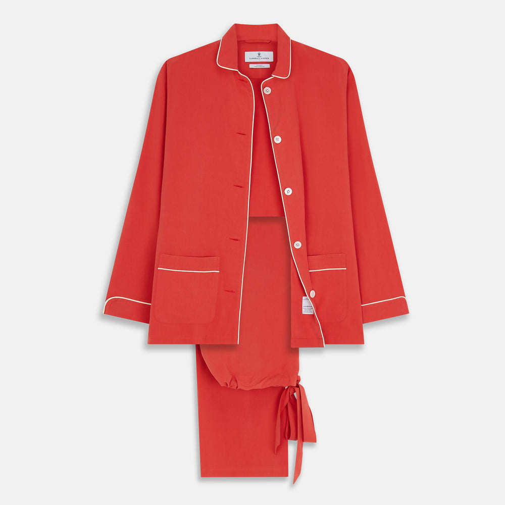 The Turnbull & Asser Women's Coral Pink Silk Thelma Pyjama Set features a long-sleeve button-up top with two front pockets and matching drawstring pants, shown on a white background.