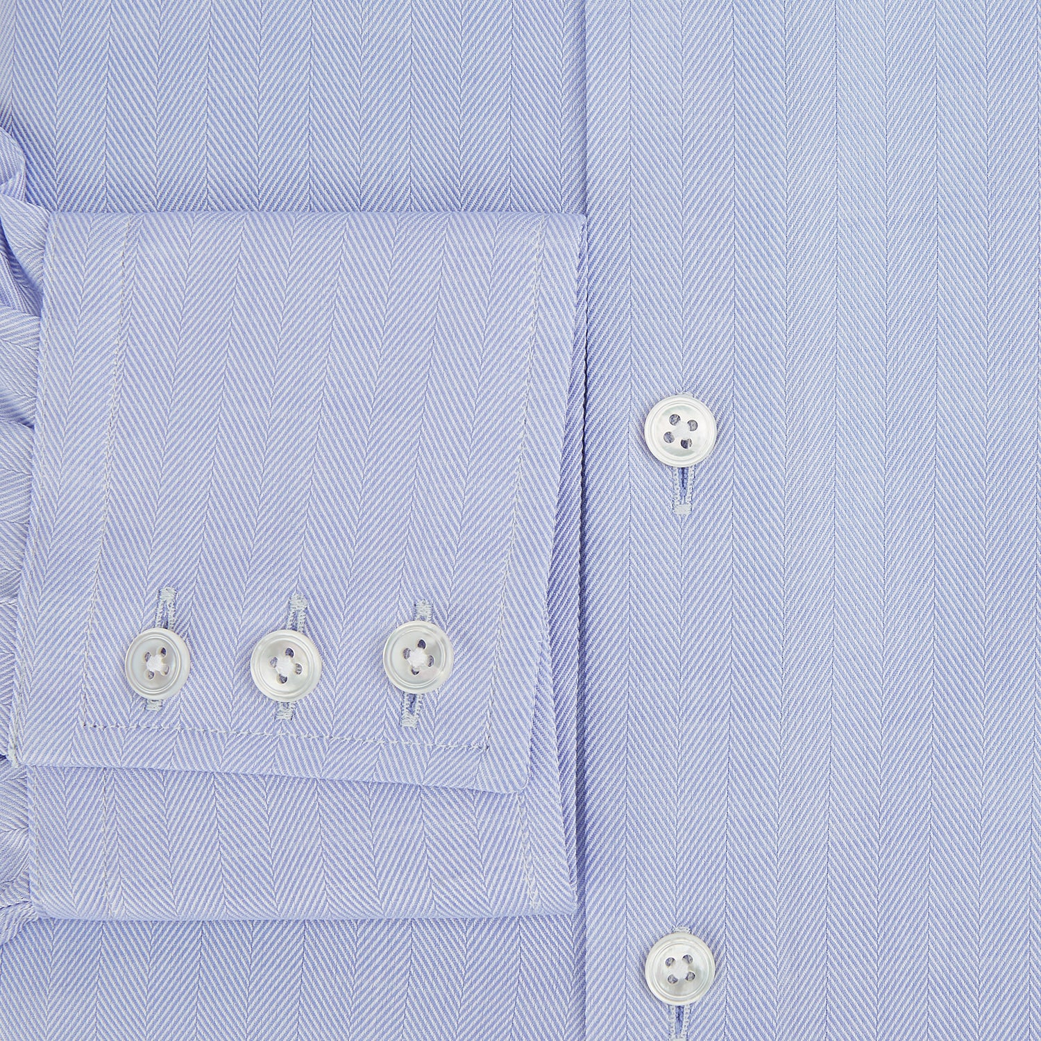 View 4 of product The Turnbull & Asser BLUE HERRINGBONE TAILORED FIT SHIRT WITH KENT COLLAR features long sleeves and buttoned cuffs, offering a timeless formal look in a classic light blue herringbone fabric, laid flat on a white background.