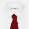 View 2 of product The Turnbull & Asser KNITTED RED SILK PLAIN TIE, featuring a textured finish, is rolled up and displayed against a plain white background.