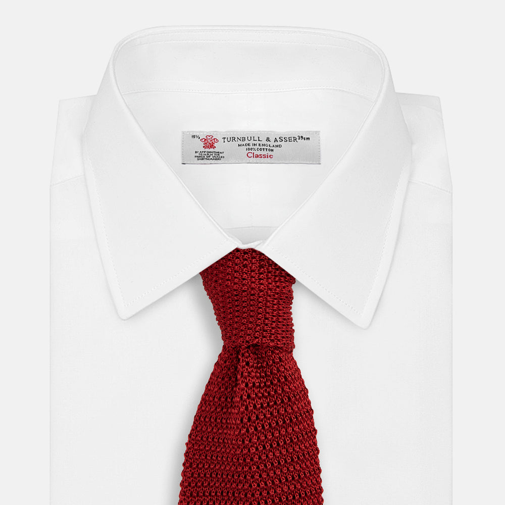 The Turnbull & Asser KNITTED RED SILK PLAIN TIE, featuring a textured finish, is rolled up and displayed against a plain white background.