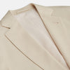 View 5 of product A man in a Turnbull & Asser Beige Cotton Barrington Blazer, light yellow shirt, blue patterned tie, and dark trousers stands against a plain light background, with a pocket square visible and a neutral expression.