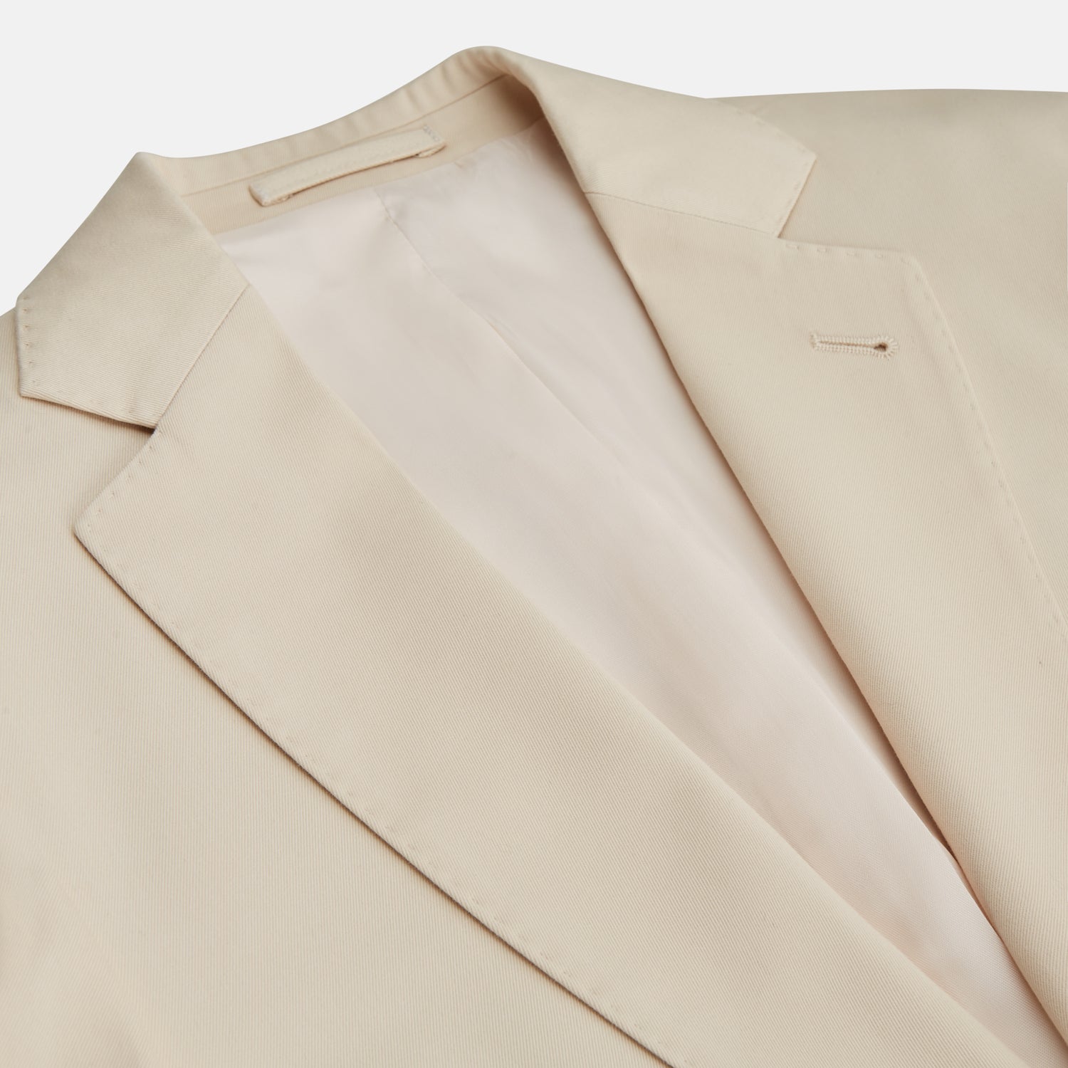 View 5 of product A man in a Turnbull & Asser Beige Cotton Barrington Blazer, light yellow shirt, blue patterned tie, and dark trousers stands against a plain light background, with a pocket square visible and a neutral expression.