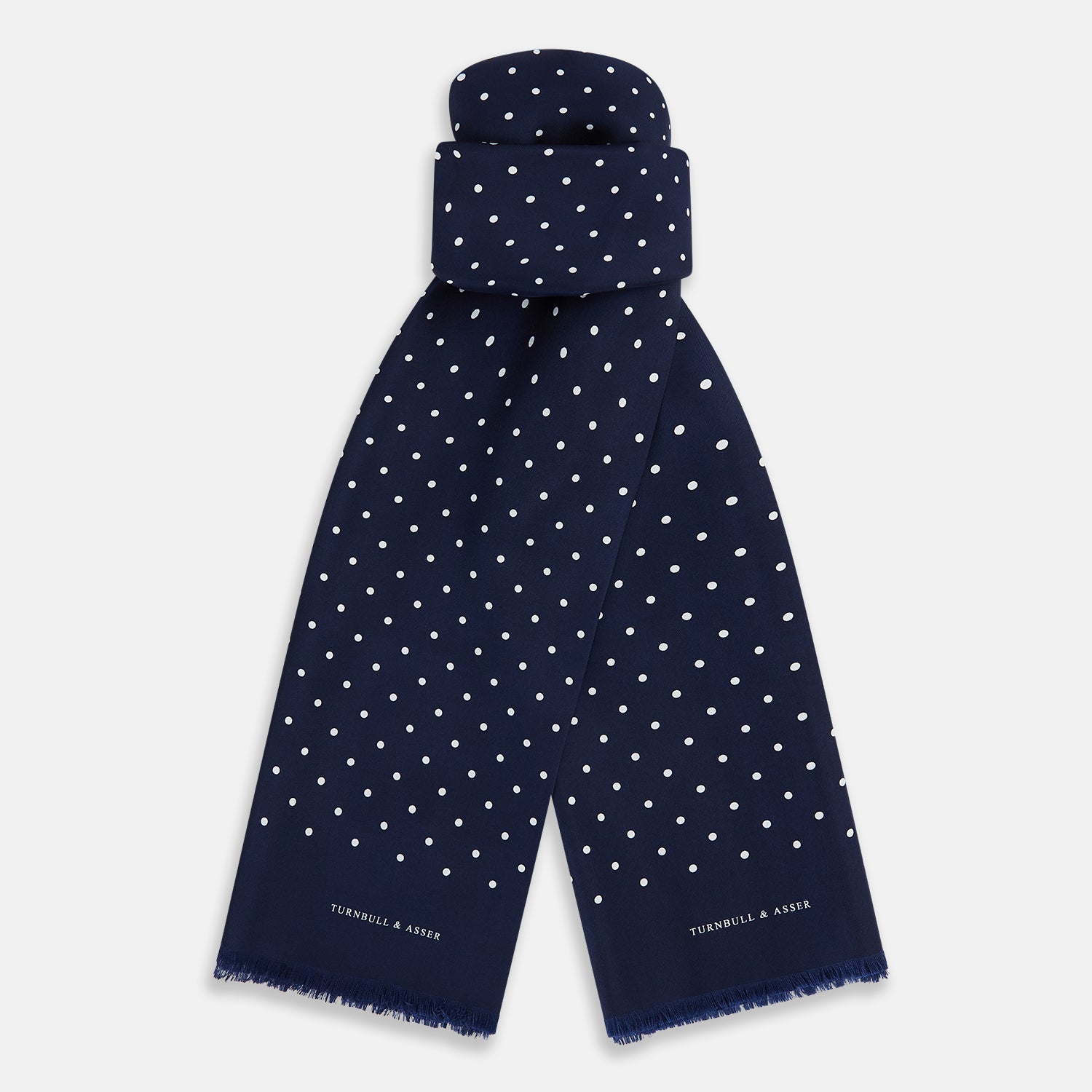 View 1 of product The Navy and White Spotted Silk Scarf by Turnbull & Asser features white polka dots, a fringed edge, and the brand's name printed near the bottom on both sides. It is neatly folded at the top.