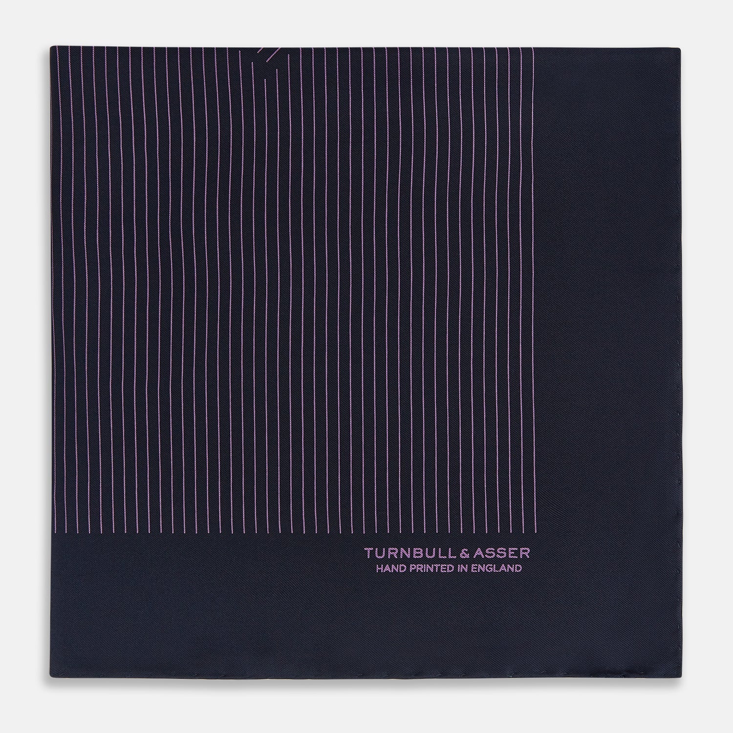View 3 of product A navy silk pocket square with thin, even purple stripes and hand-rolled edges from Turnbull & Asser, featuring "Turnbull & Asser Hand Printed in England" printed in the corner.