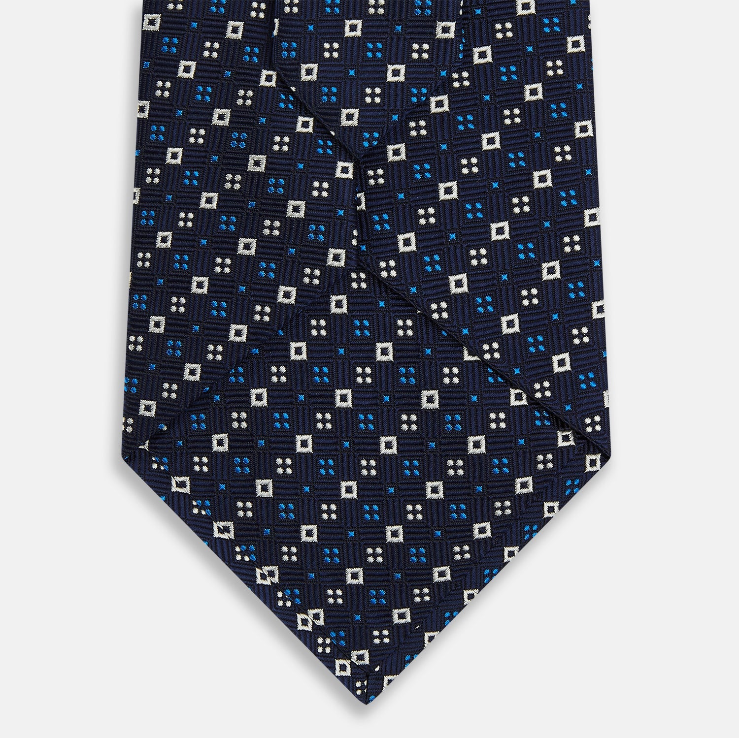 View 3 of product The Blue and White Geometric Silk Tie by Turnbull & Asser, featuring a pattern of small squares and dots, is shown rolled up against a plain white background.