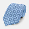 View 1 of product The Turnbull & Asser Blue Floral Tile Pattern Printed Silk Tie features a light blue geometric and floral design in dark blue, shown rolled up on a white background.