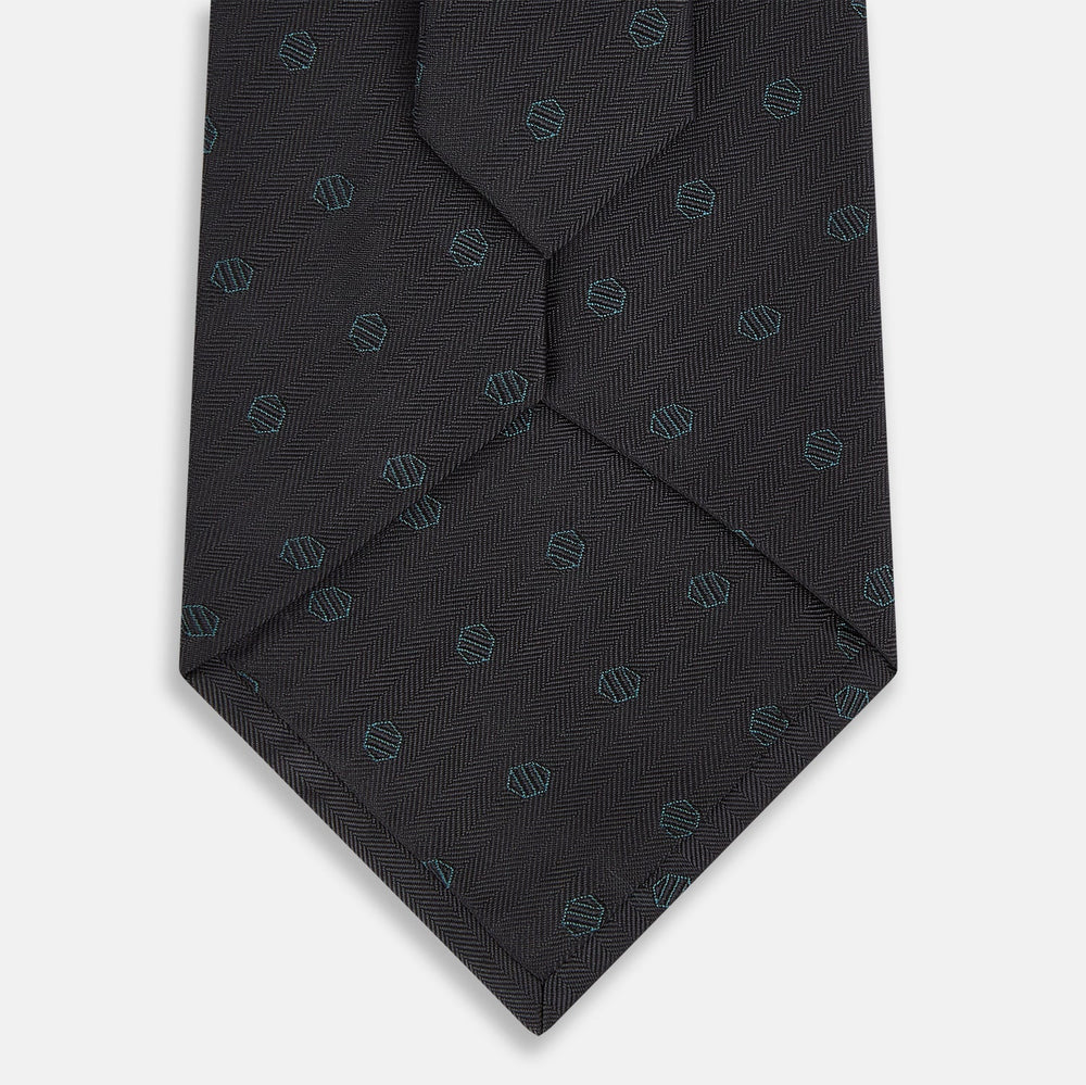 The Turnbull & Asser Teal and Navy Circle Silk Tie features a subtle herringbone pattern with small repeating circle motifs, displayed neatly rolled on a white background.