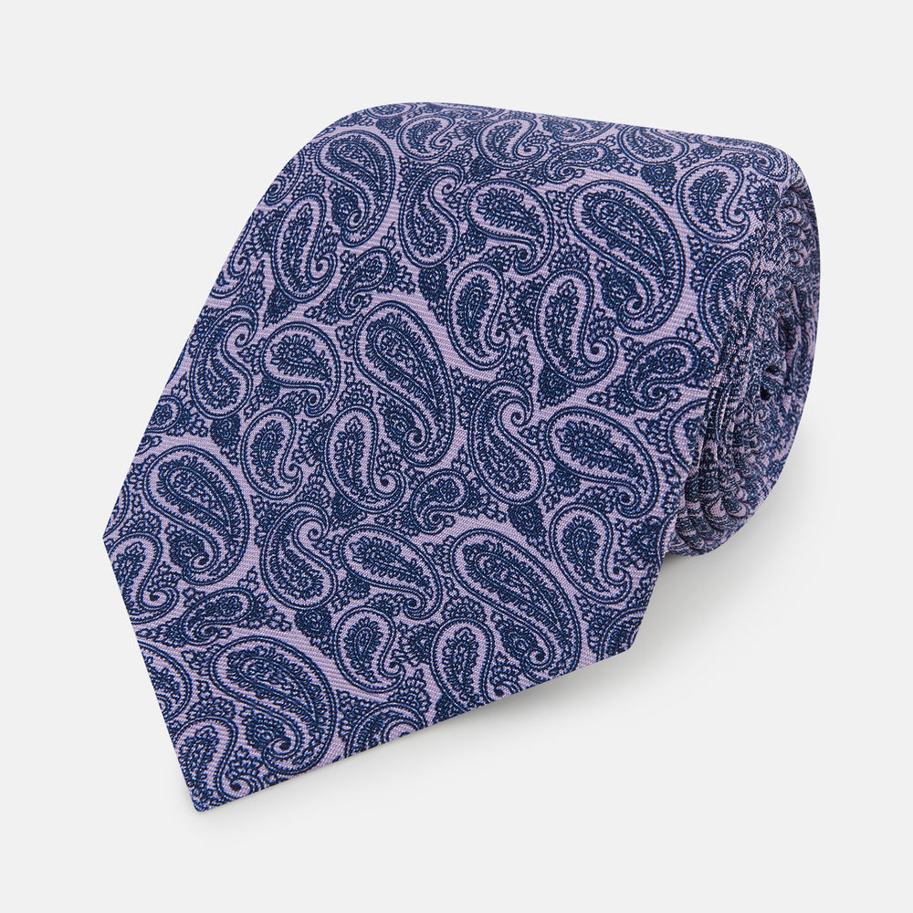The Turnbull & Asser Lilac Paisley Silk Tie, crafted in England, features a blue paisley pattern on a lilac background and is shown rolled up against a white surface.