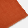 View 2 of product The Rust Cashmere Scarf by Turnbull & Asser is hand-dyed in rust-orange, made from lightweight fabric, tied loosely at the top with both ends hanging down, and finished with subtle frayed edges against a plain white background.