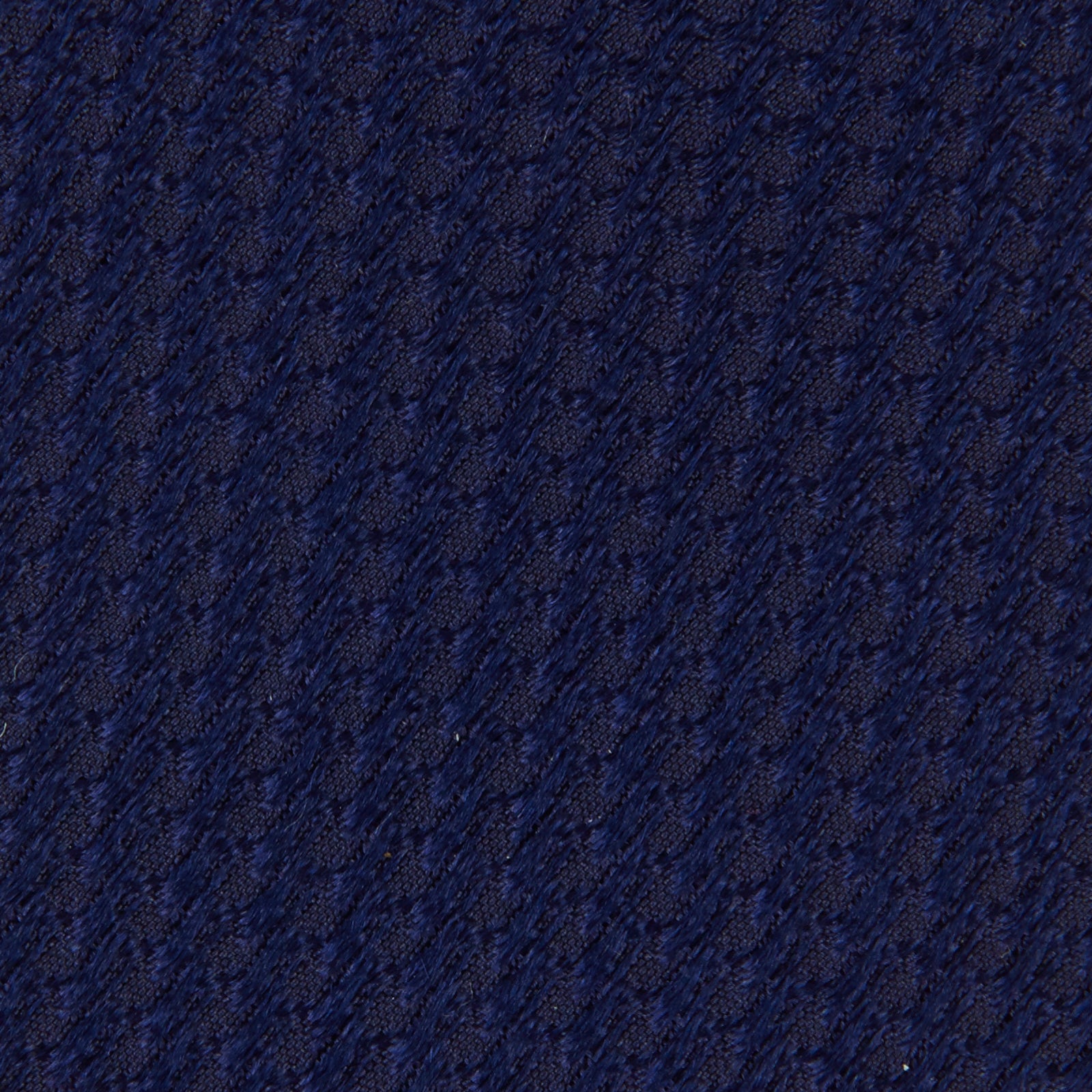 View 3 of product The Turnbull & Asser Seven-Fold Navy Lace Silk Tie is shown on a white background, rolled at one end with the pointed tip facing forward.