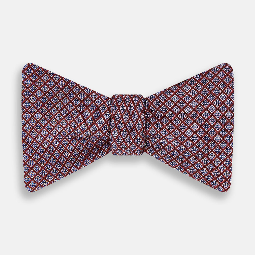 The Indies Red Floral Square-Print Silk Bow Tie by Turnbull & Asser features a geometric blue and white diamond pattern on red silk, styled against a white background for classic British elegance.